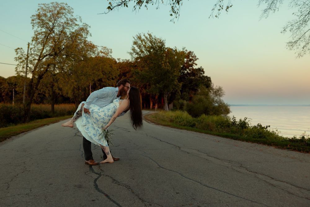 A skateboarder performs tricks on a winding road along a scenic coastal cliff at sunset.