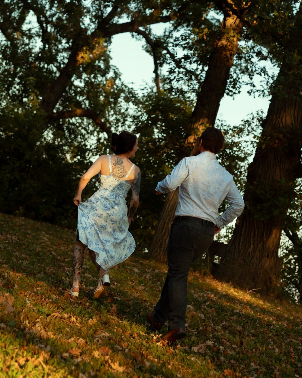A couple dances together on a hillside at sunset among tall trees creating a romantic silhouette against the golden light.