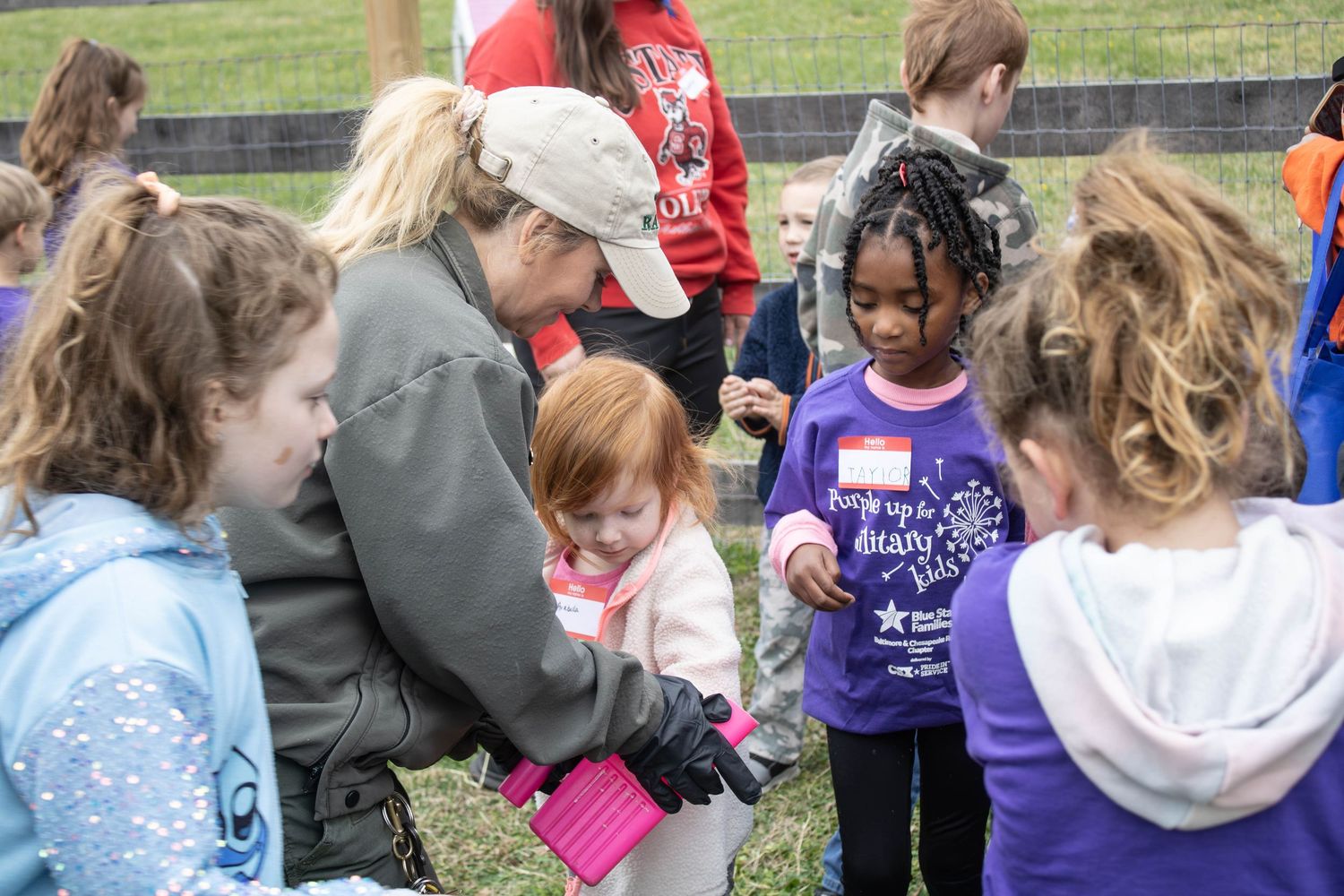 Children and adults gather outdoors at a school event, with a young girl in a purple shirt at the center.