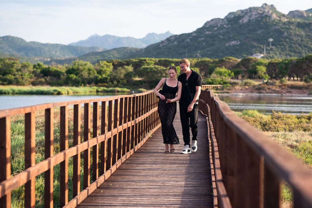 Two people strolling on elevated wooden walkway through scenic mountain wetlands.