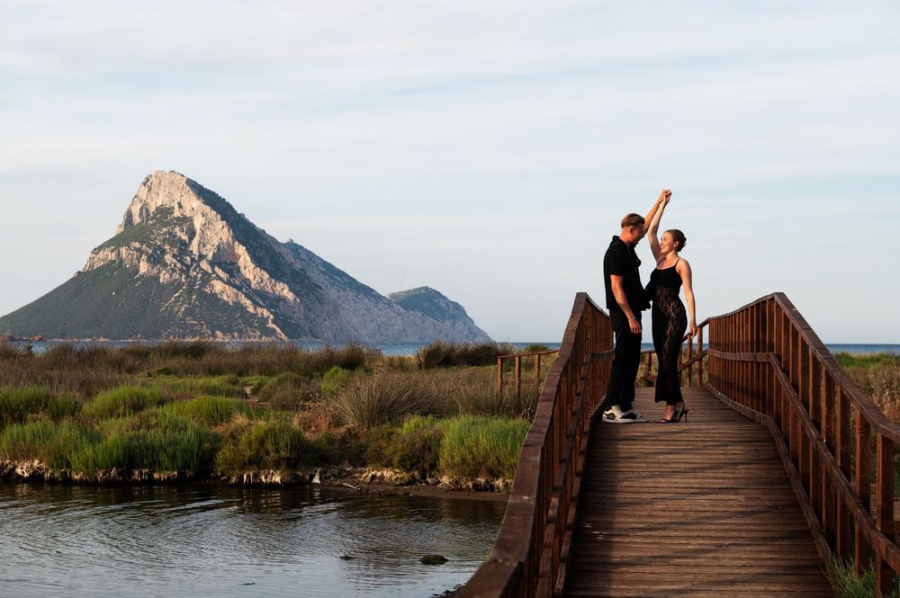 Couple posing on wooden boardwalk with dramatic mountain peak and wetlands in background.