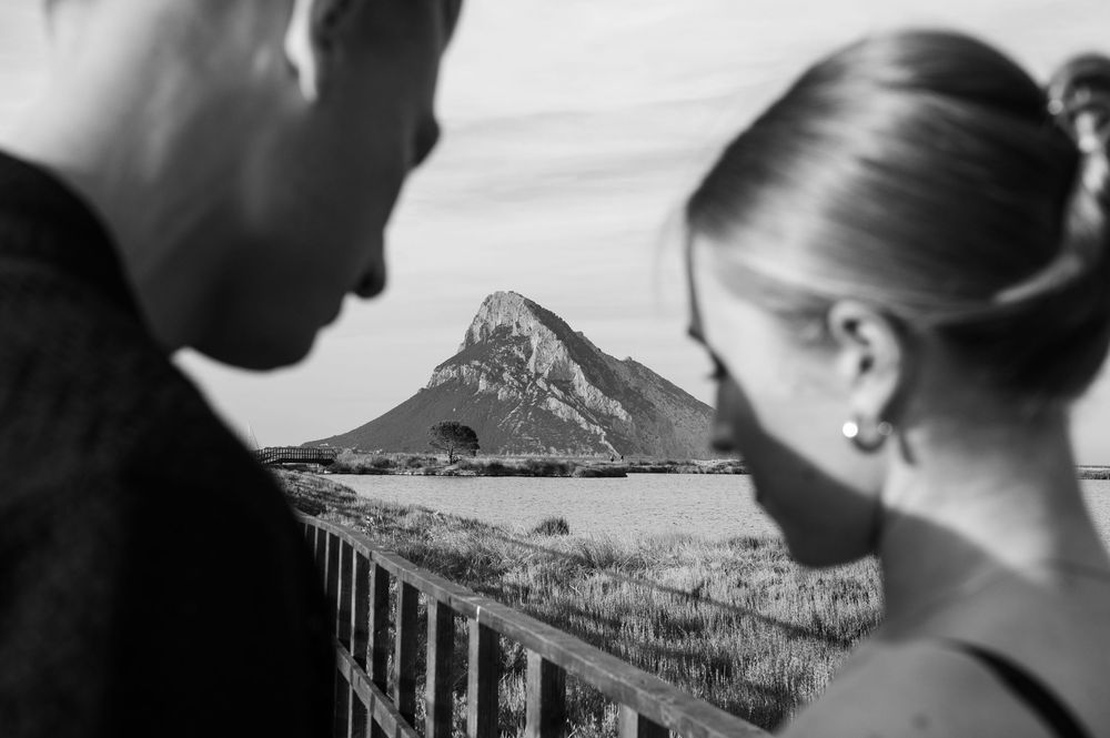 Black and white portrait of a couple with coastal mountain landscape in background.