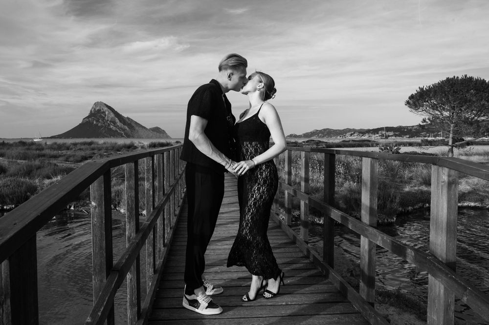 Couple walking along wooden boardwalk with dramatic coastal landscape.