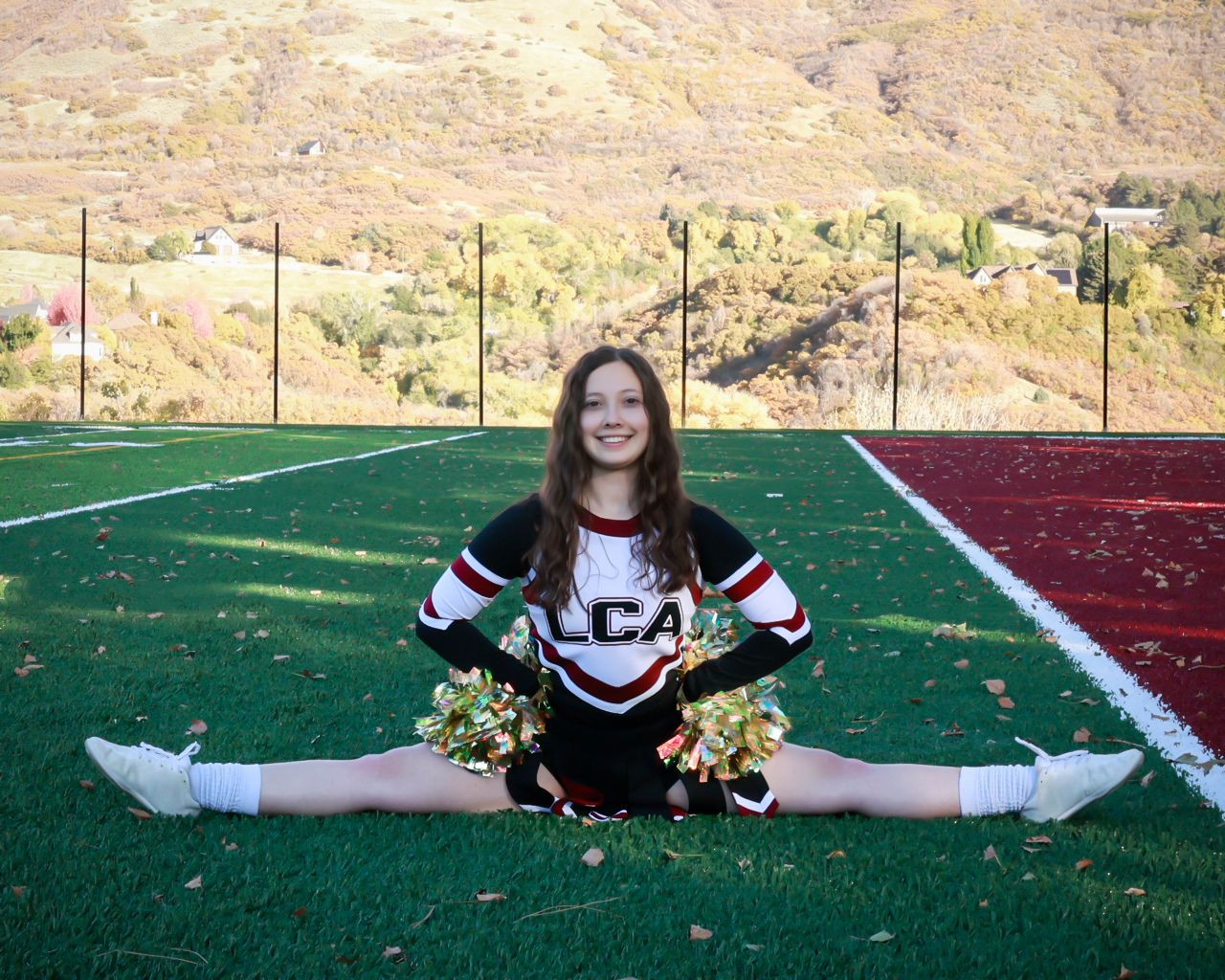 A cheerleader performs splits on a sports field with mountains visible in the background.