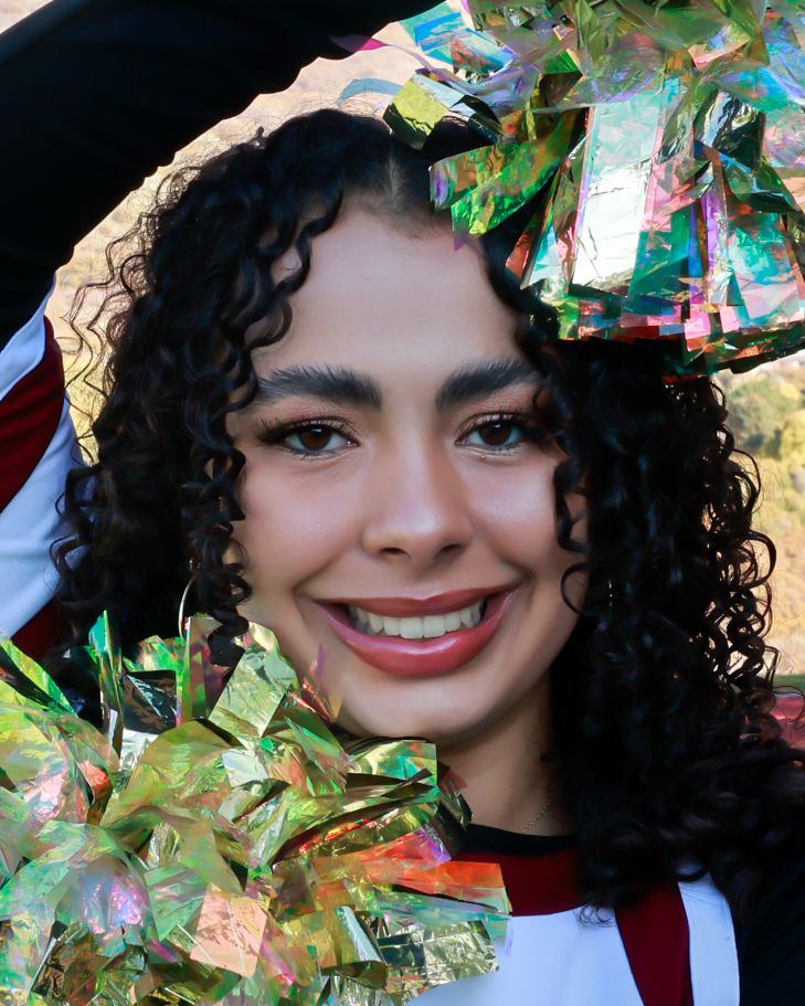 A person with curly dark hair smiles while surrounded by colorful metallic confetti and decorative elements.