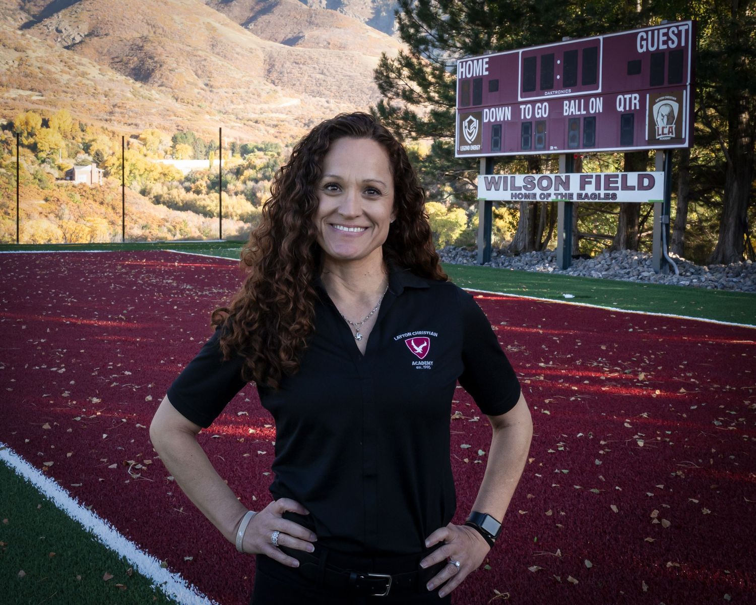 Athletic trainer stands on red track field at sunset with mountains visible in background.
