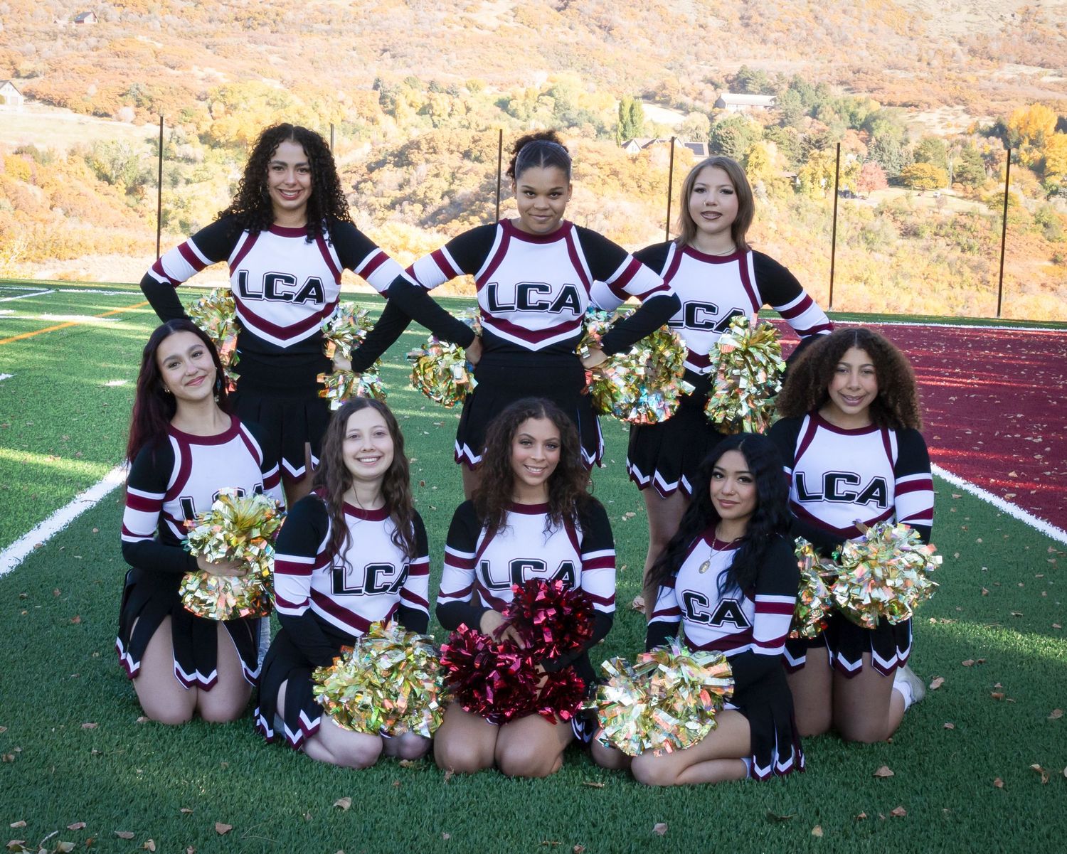 Cheerleaders in black and white uniforms pose together on a sports field with pom poms.
