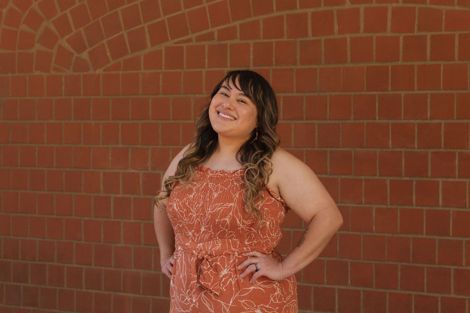 Cristina Sosa in orange floral lined jumper smiling for Life Path Coaching business headshots in front of brick wall in Downtown Spokane