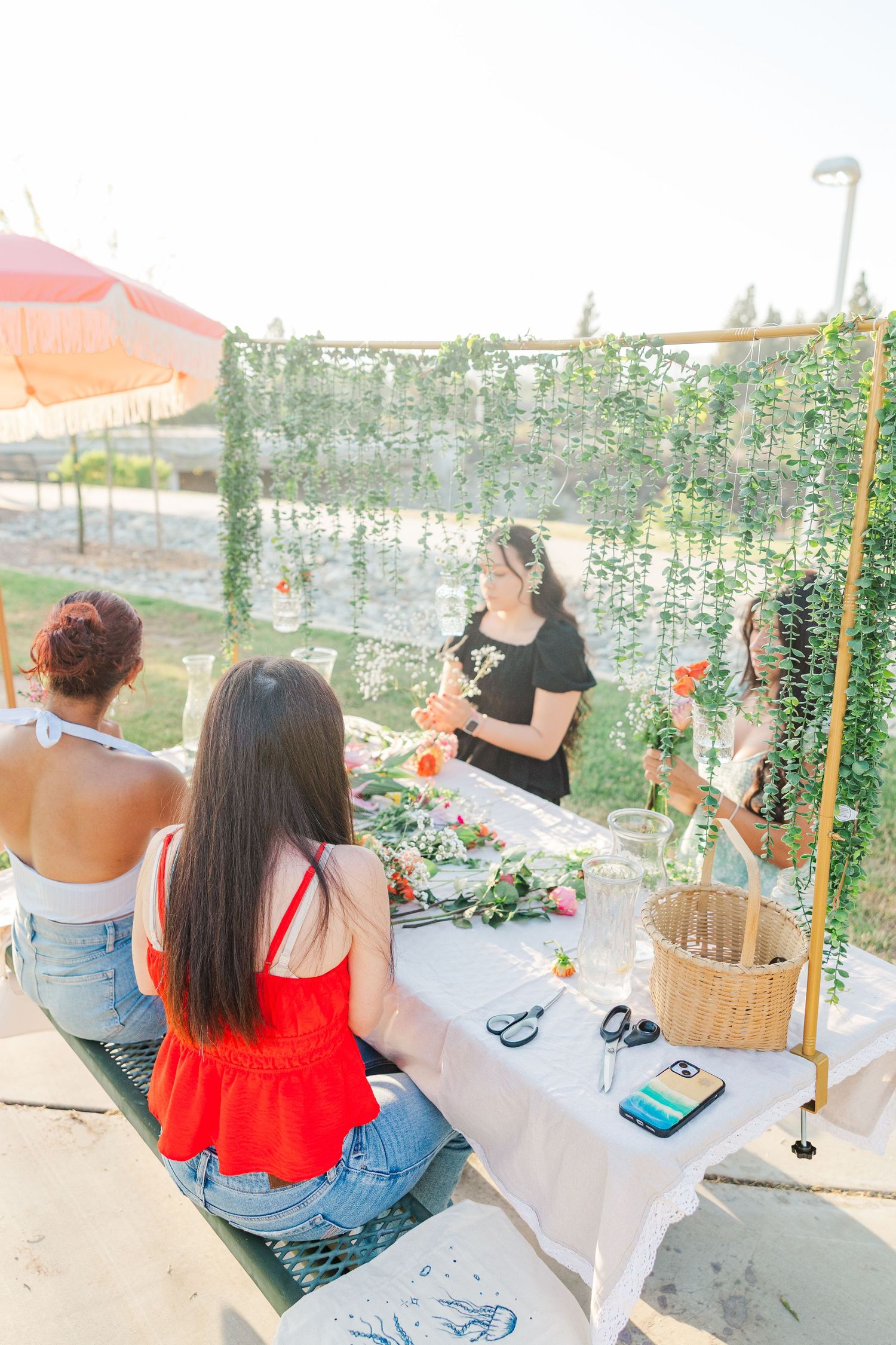 Friends enjoying a relaxing outdoor gathering with hanging decorations and string lights in a garden setting.