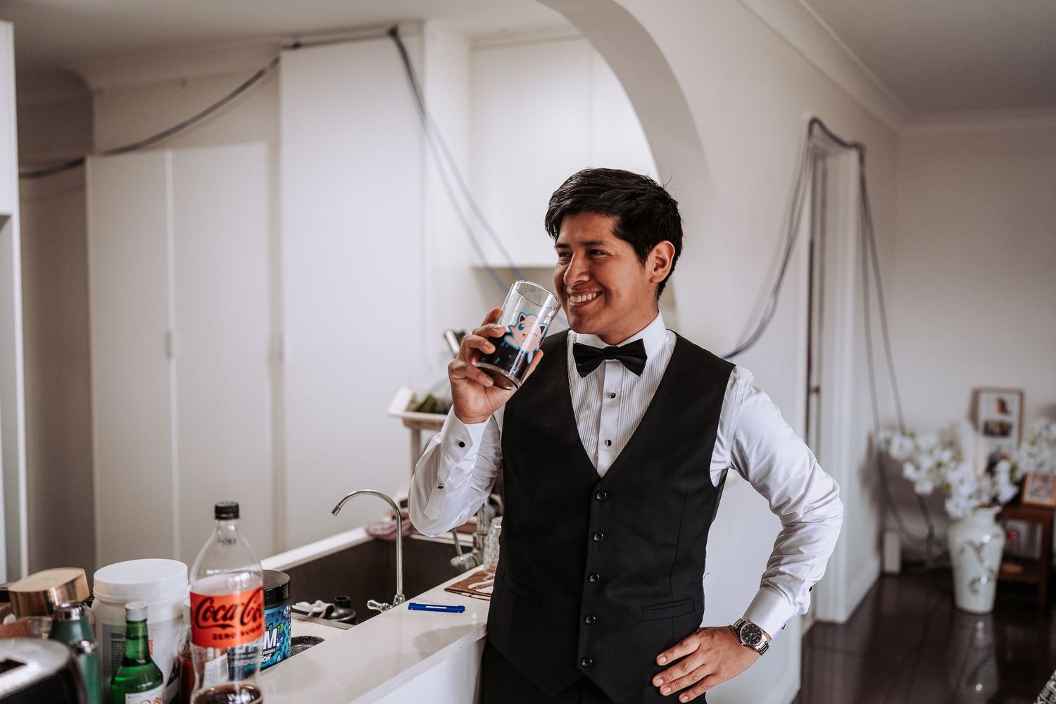 A person in formal attire stands at a bar counter with wine glasses and beverages in an elegant setting.