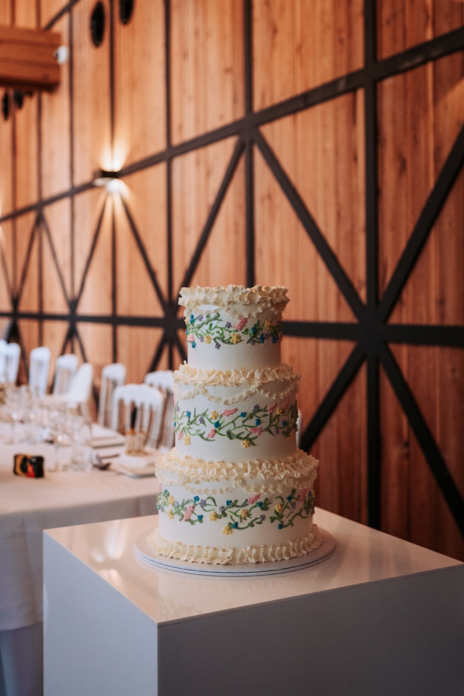 Three-tiered white wedding cake with delicate blue floral details displayed in a rustic wooden barn venue.