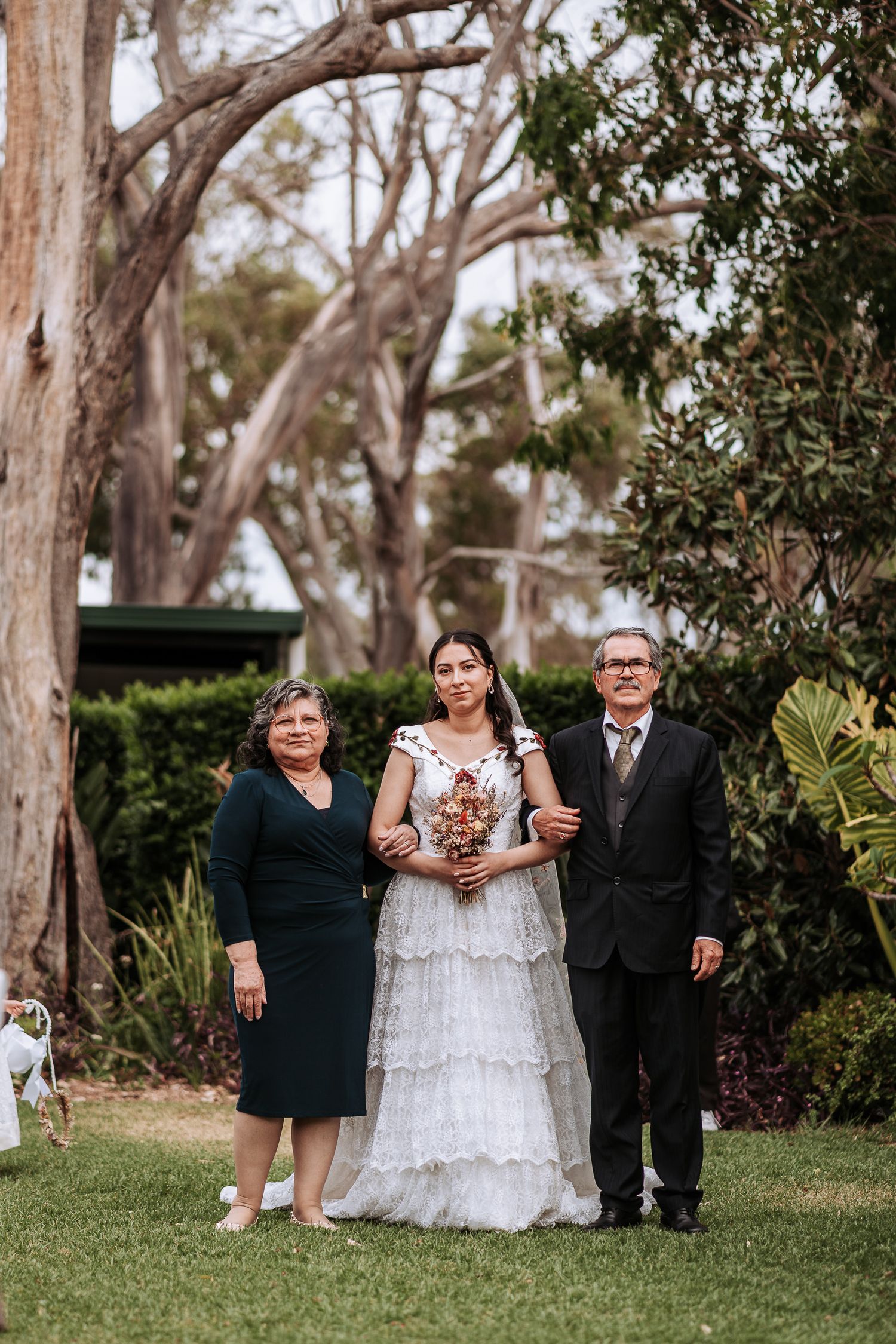 A wedding portrait outdoors with a beautiful white lace gown and family members against a backdrop of eucalyptus trees.