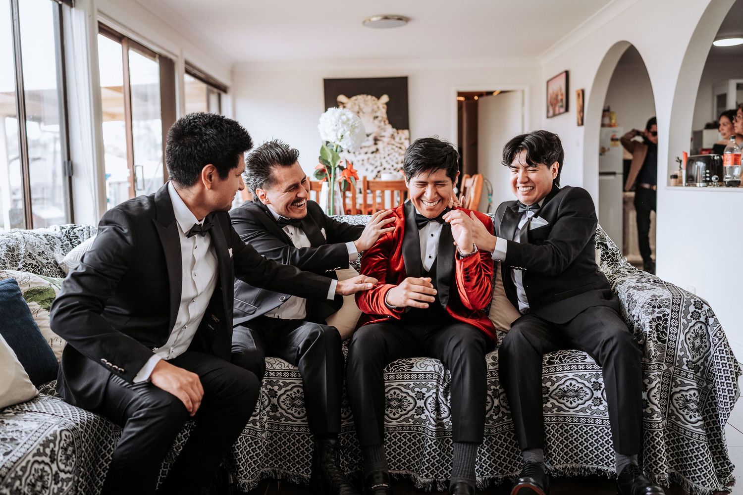 A group of people in formal attire sit on a patterned couch while laughing and socializing together.