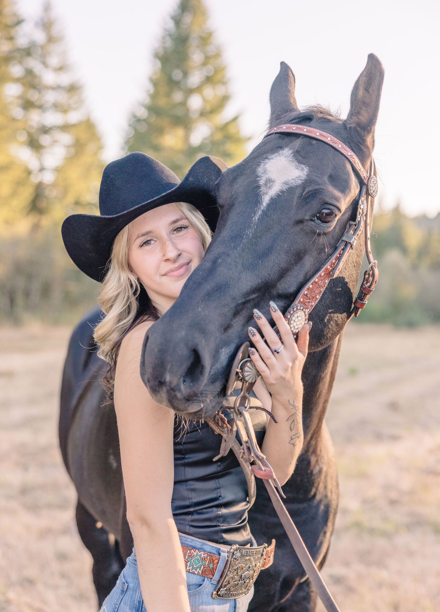 Person in cowboy hat posing with black horse in outdoor setting.