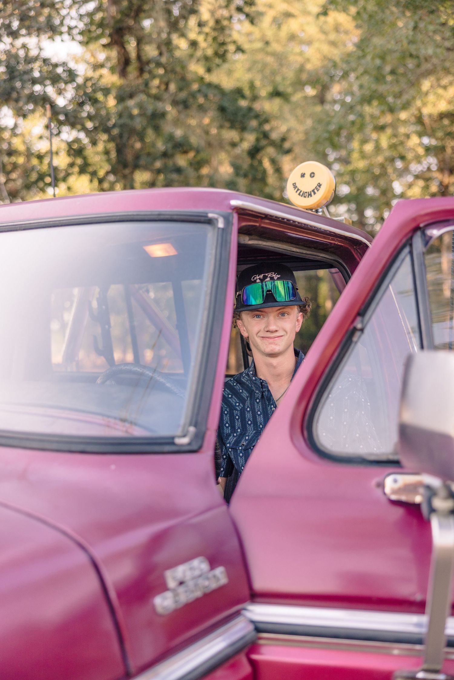 People sitting in a vintage burgundy car with sunlight filtering through.