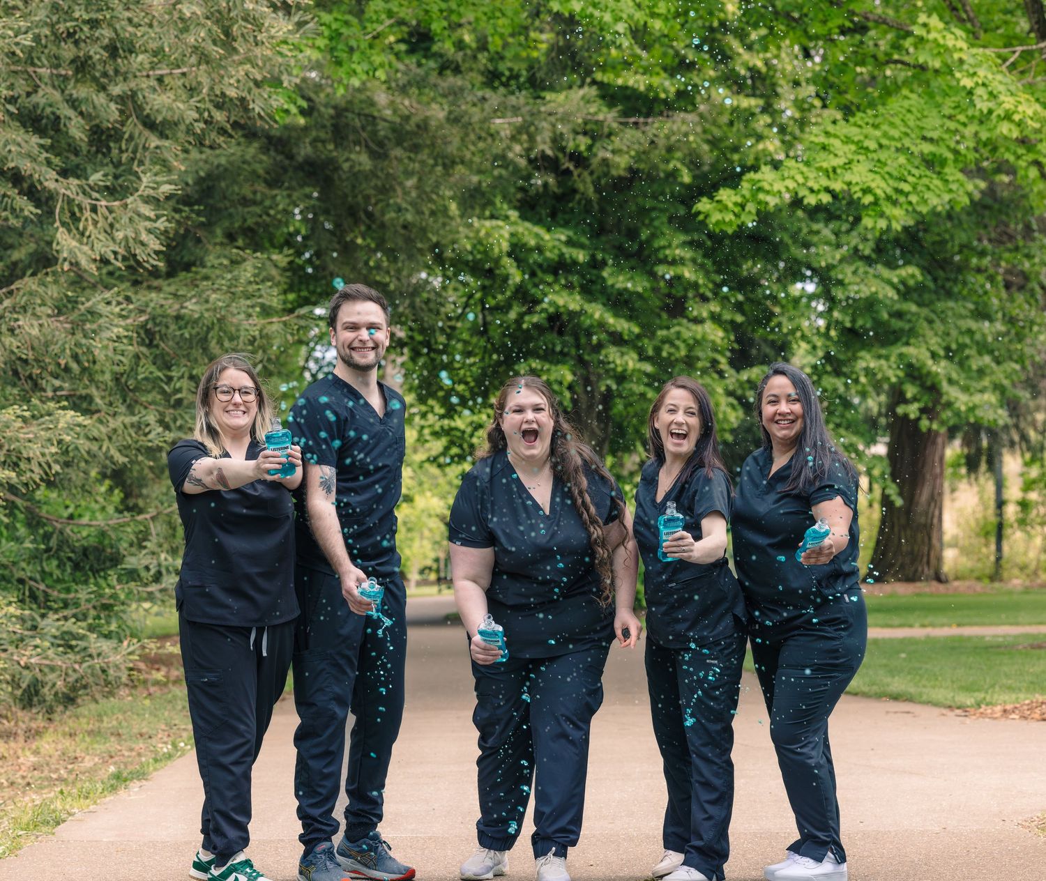 Group of friends in dark outfits playfully toss water during an outdoor photoshoot.