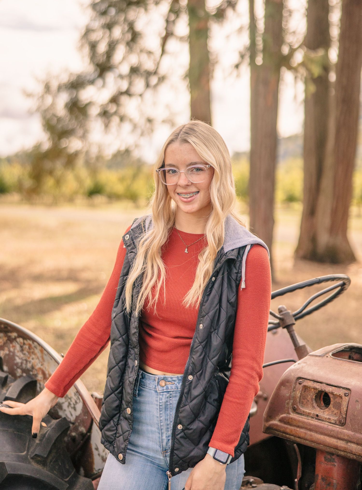 Person in red sweater and denim sitting on vintage tractor in forest setting.