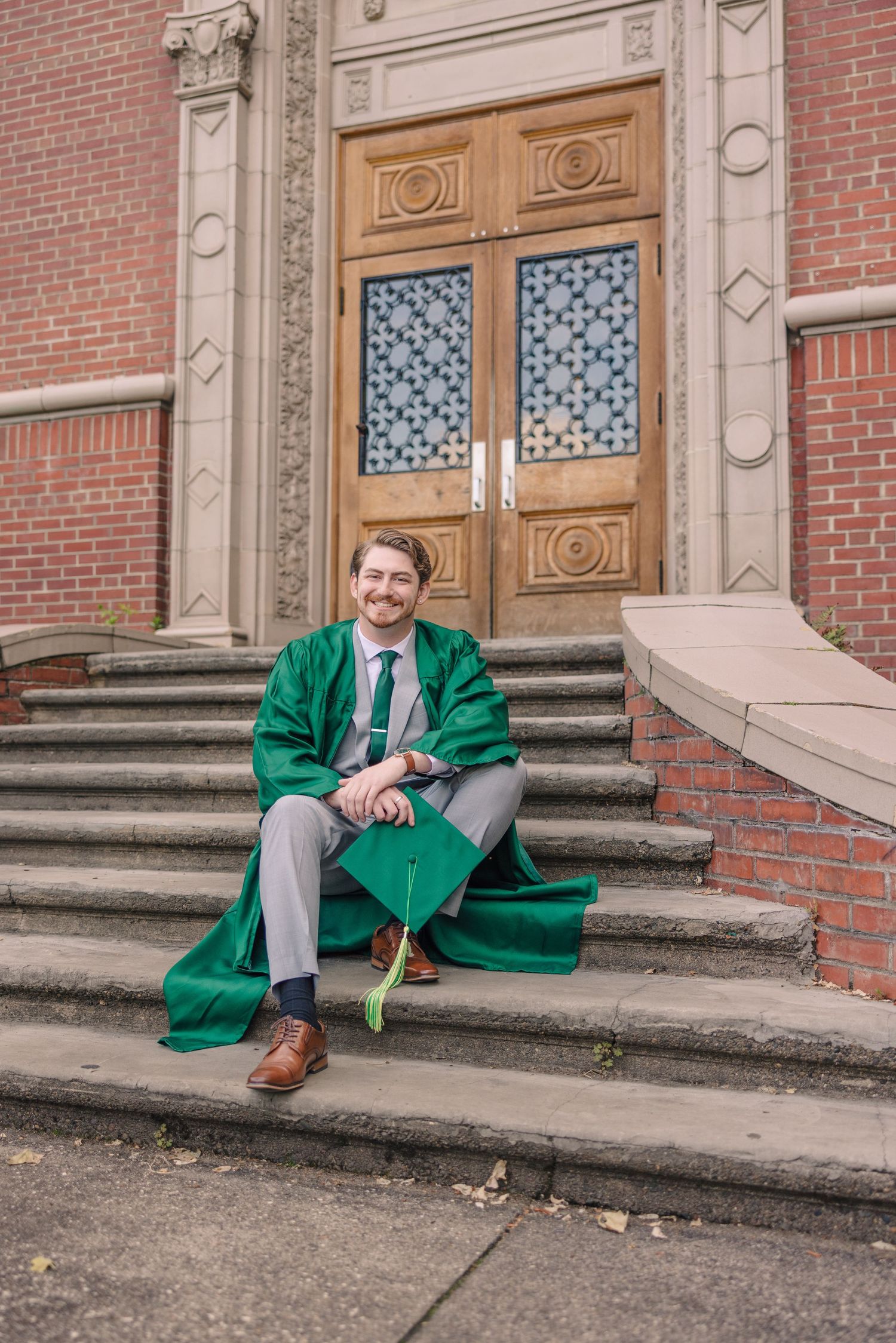 Person in a bright green blazer sitting on brick steps in front of ornate wooden doors.