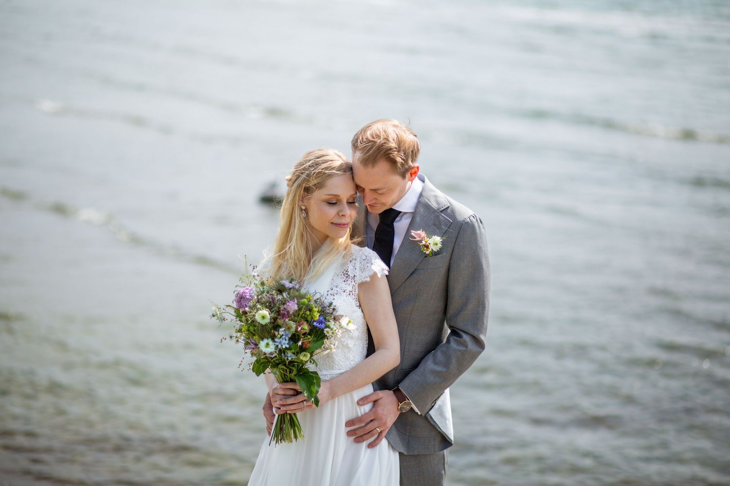 A couple embraces on a misty beach with rolling waves in the background during their wedding photoshoot.
