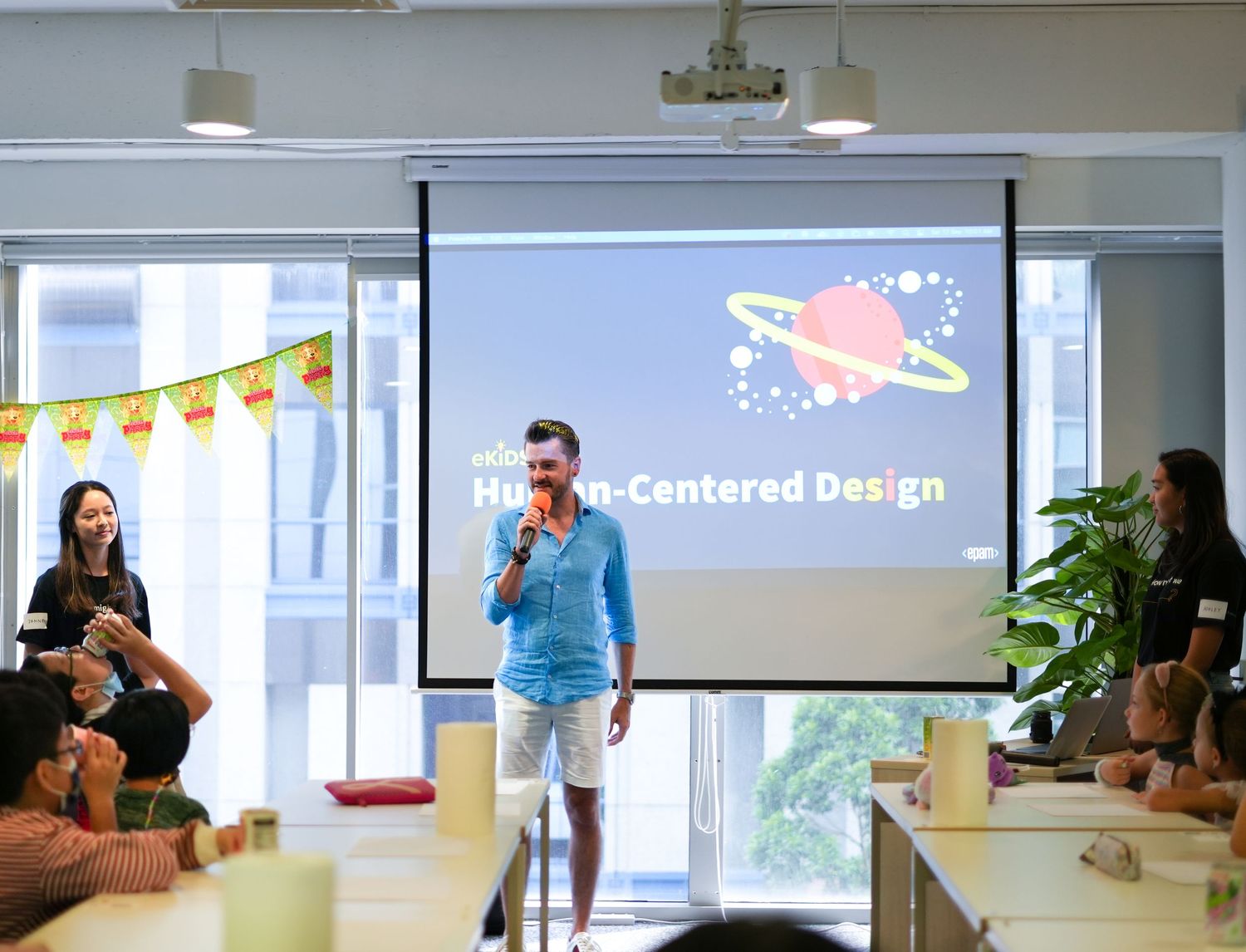 Excited graduates in blue gowns celebrate by raising their arms in front of a school building.