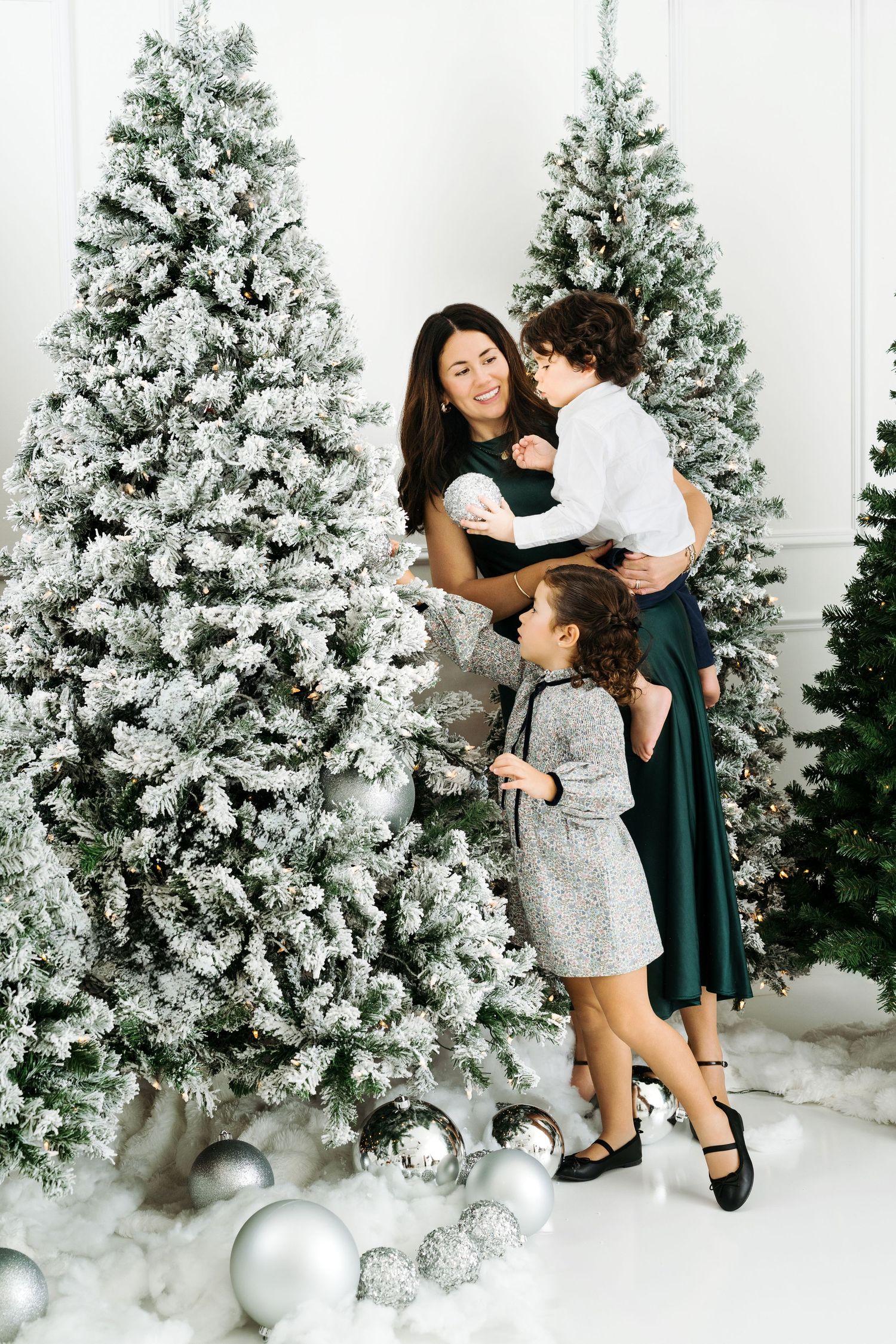 Mom and kids are decorating Christmas tree with ornaments at frosted tree setup
