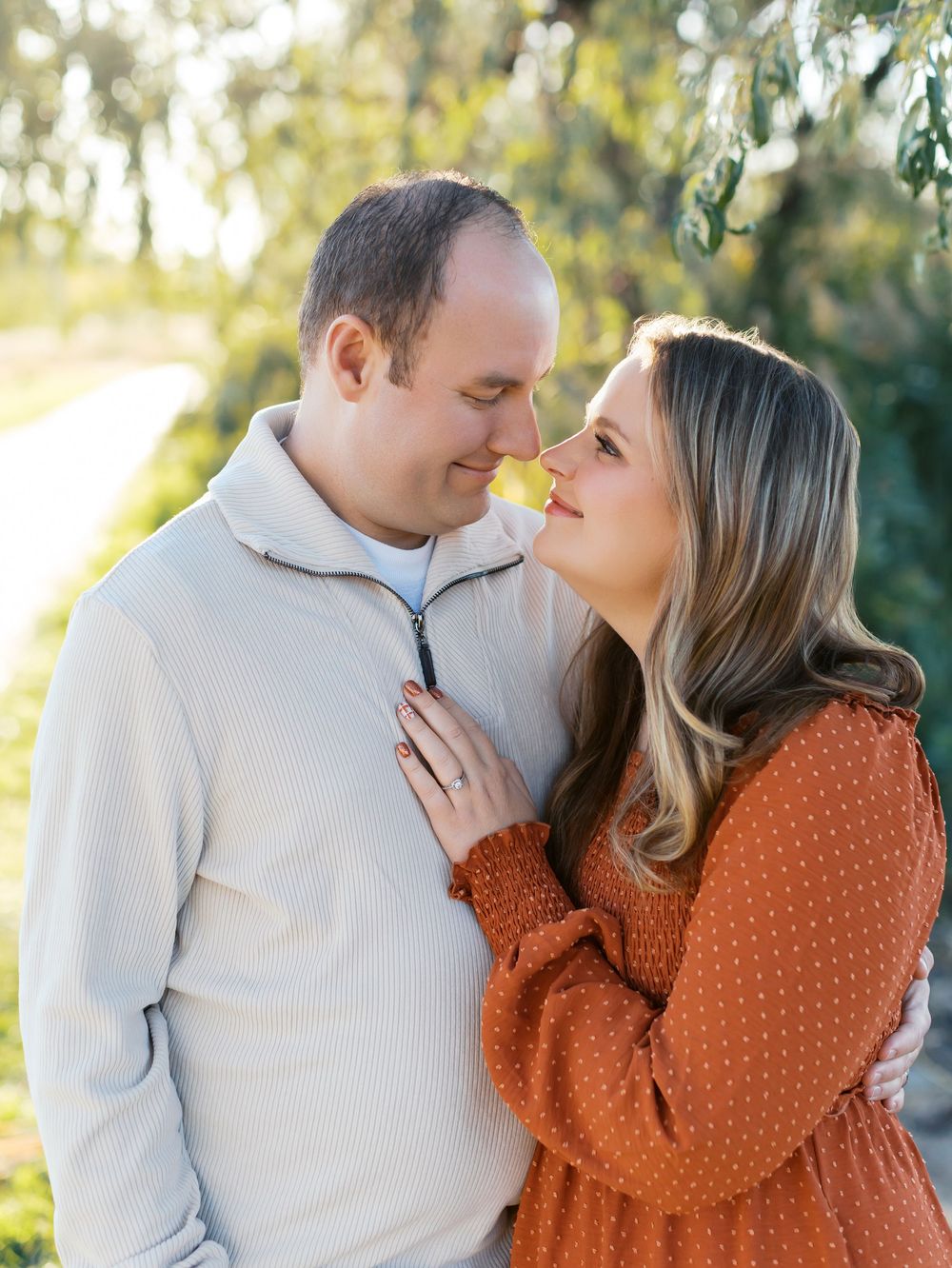 A couple shares tender moments in a sunlit outdoor setting wearing orange and white outfits.
