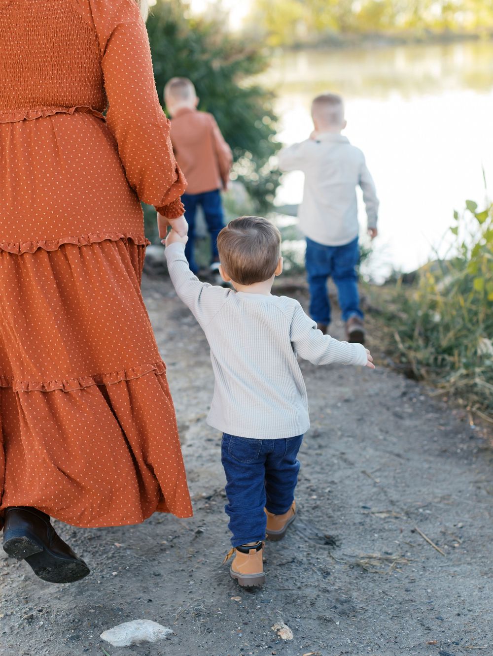 A parent and children walk together on a dirt path near a lake during golden hour.