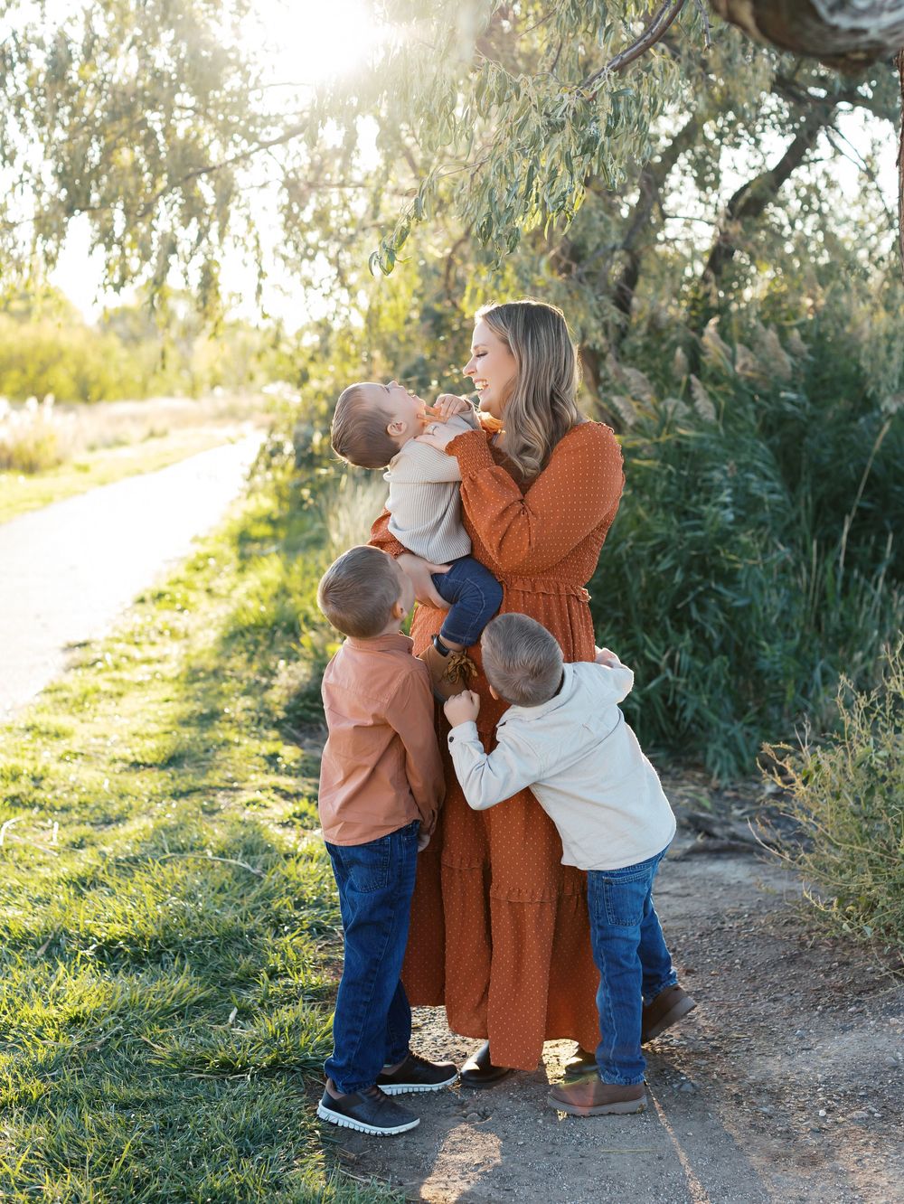 A family shares a joyful moment together on a sunlit nature path with golden light filtering through trees.