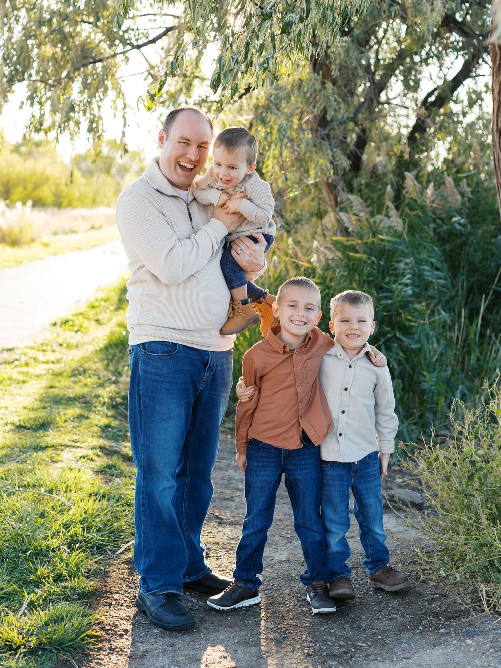Family group wearing coordinated casual outfits poses together on outdoor path near trees.