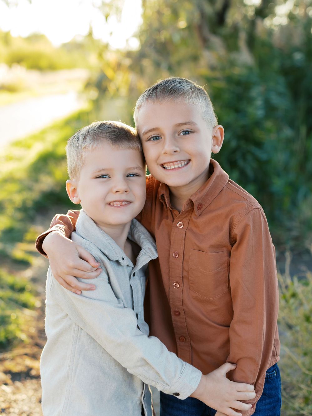 Two children in button-up shirts share a warm embrace while posing outdoors in natural lighting.