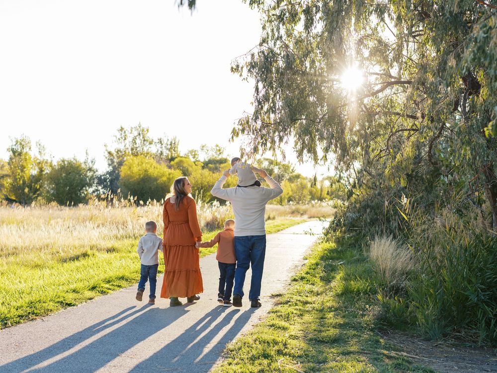 Silhouettes of a family walking together on a path at sunset with long shadows cast on the ground.