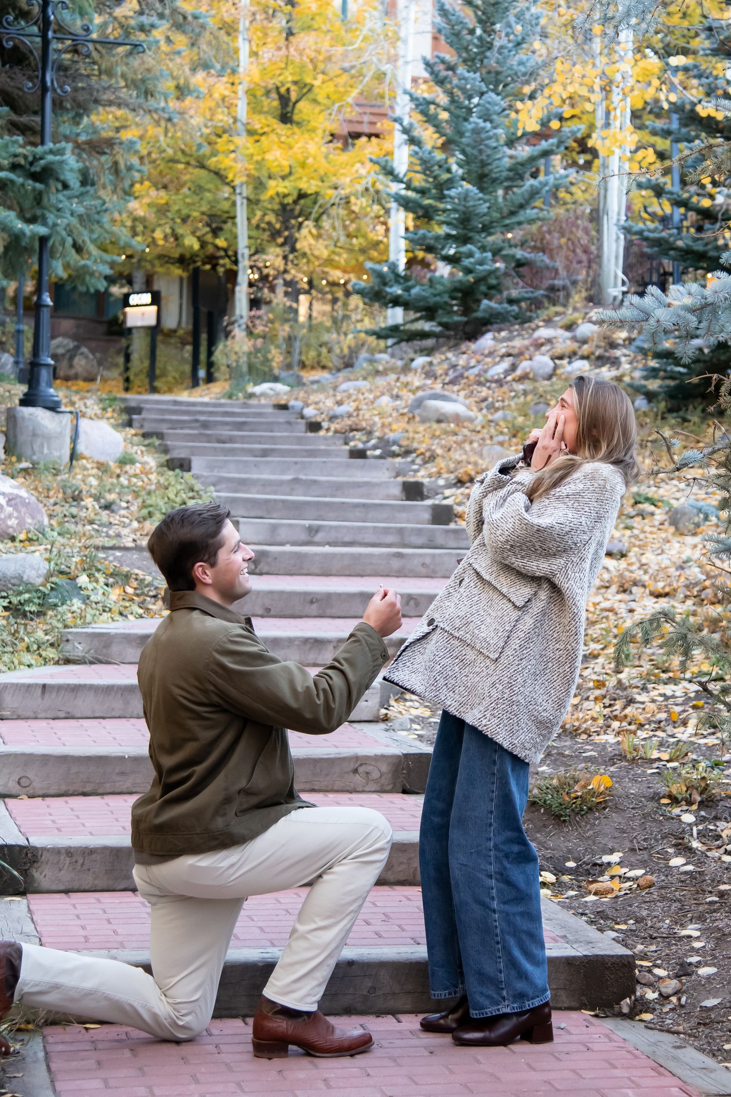 A romantic marriage proposal scene unfolds on outdoor stone steps surrounded by autumn foliage in Vail Colorado.
