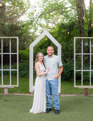 Couple walking together on grass near decorative white window frames in an outdoor setting.