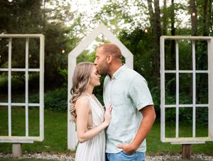 A romantic couple shares tender moments in a garden setting with white architectural elements in the background.