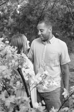 A romantic couple poses among white blossoms in a natural outdoor setting.