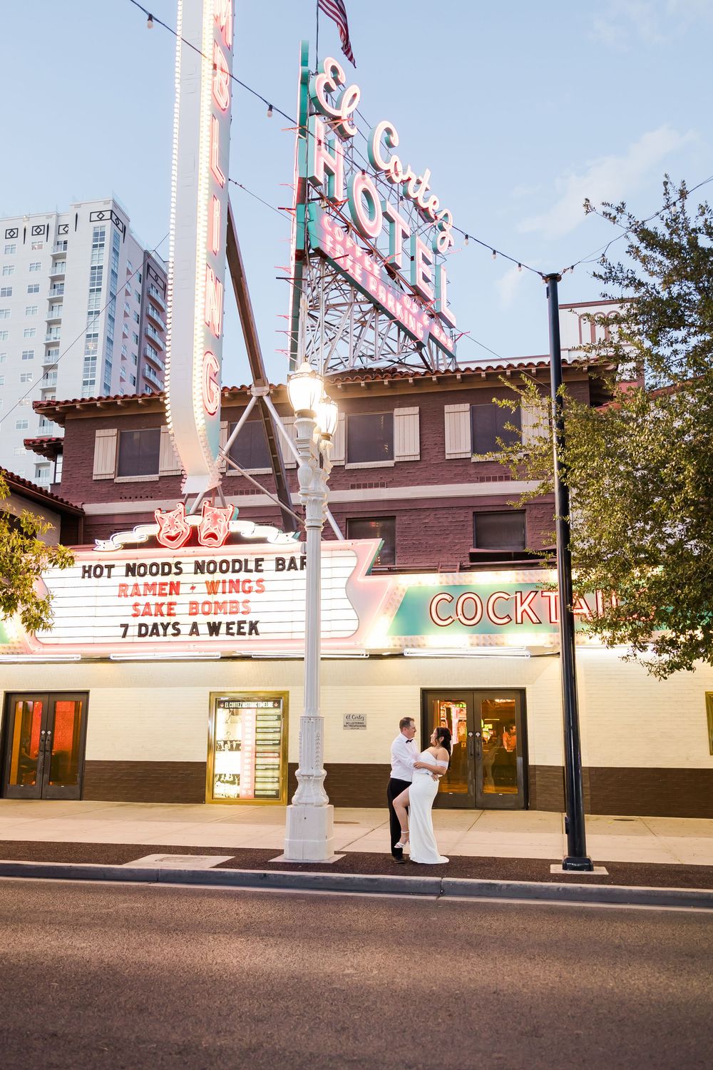 Wedding couple takes romantic photos in front of a retro noodle bar and cocktail lounge at dusk.