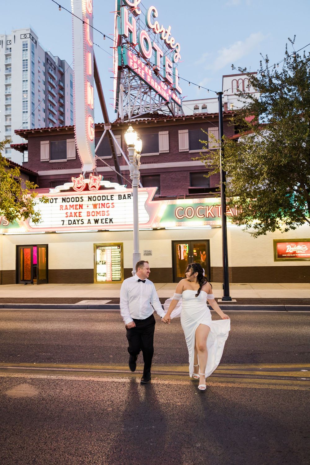 A couple in formal attire poses for romantic photos in front of a vintage movie theater marquee at dusk.