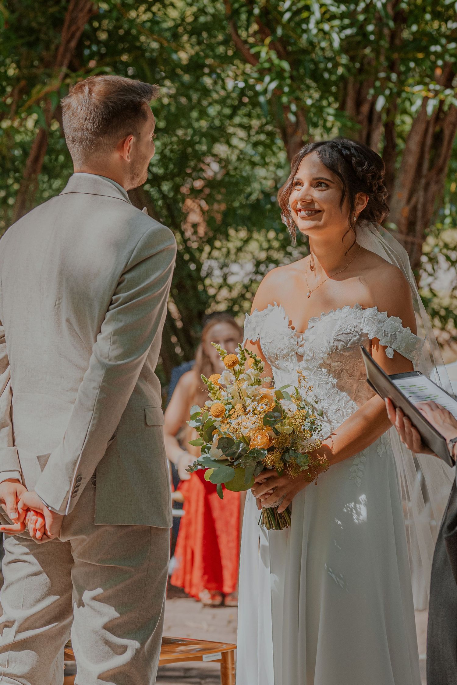 A romantic couple in white clothing shares an intimate moment in a wooded setting during golden hour.