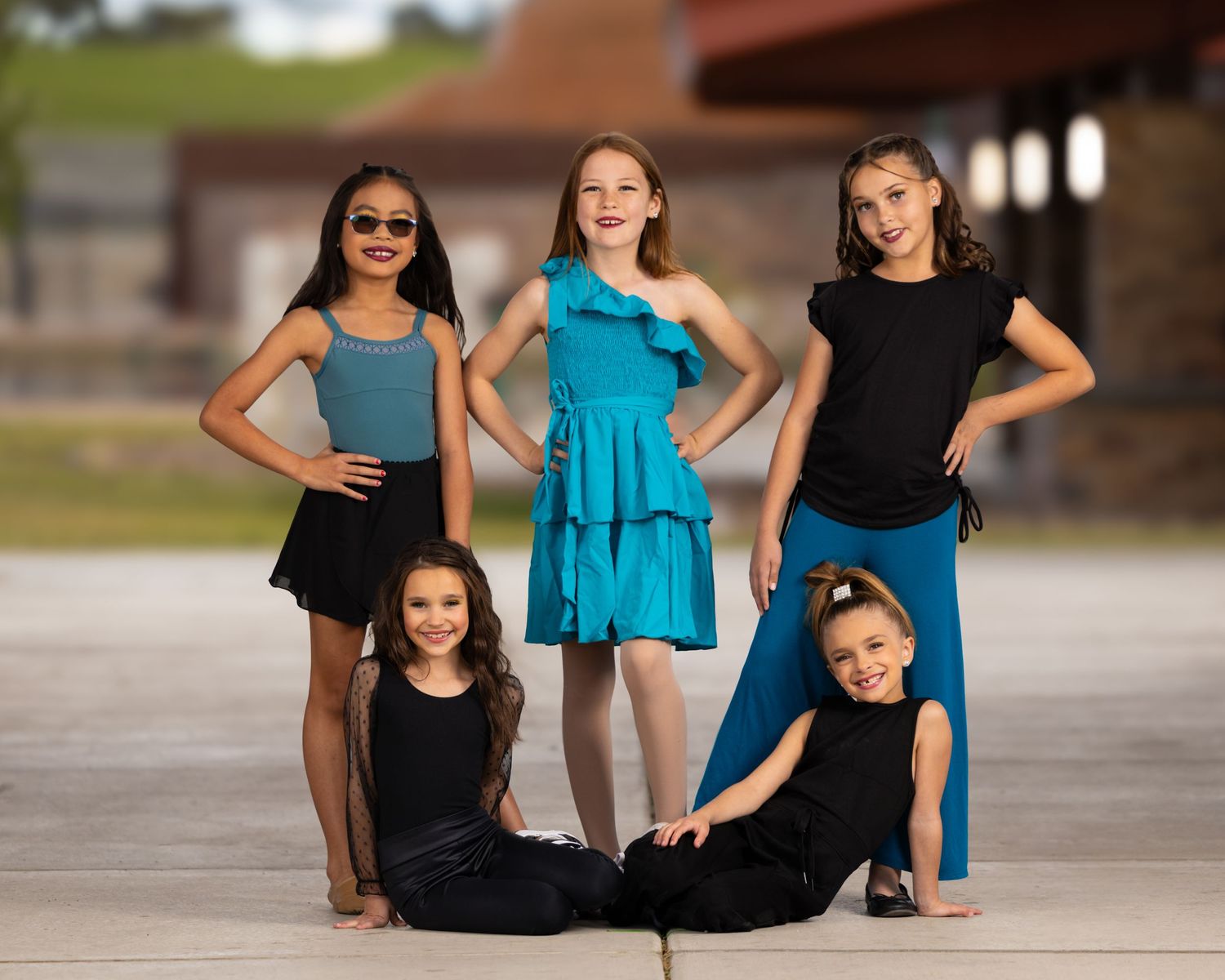 Two dancers wearing black and turquoise leotards pose gracefully on a concrete stage during a dance performance session.