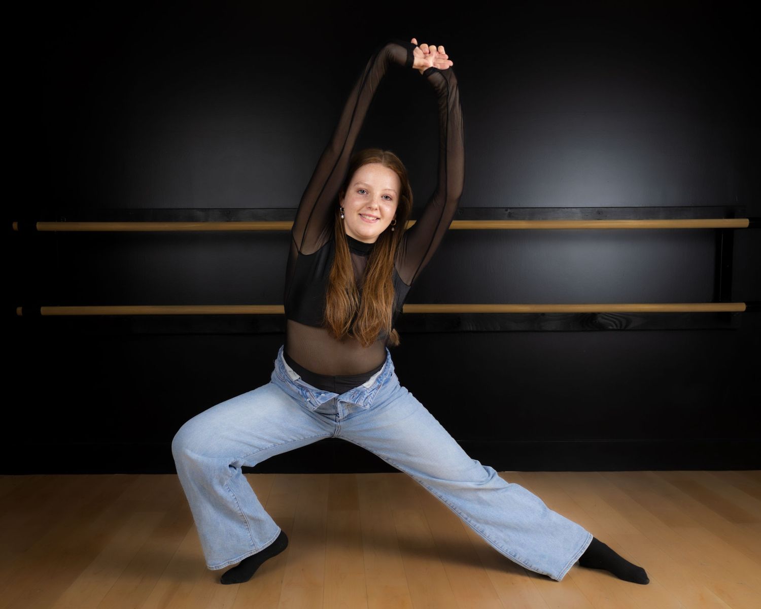 A sequence of ballet dance poses showing leg movements and stretches across a dark studio space with wooden bars.