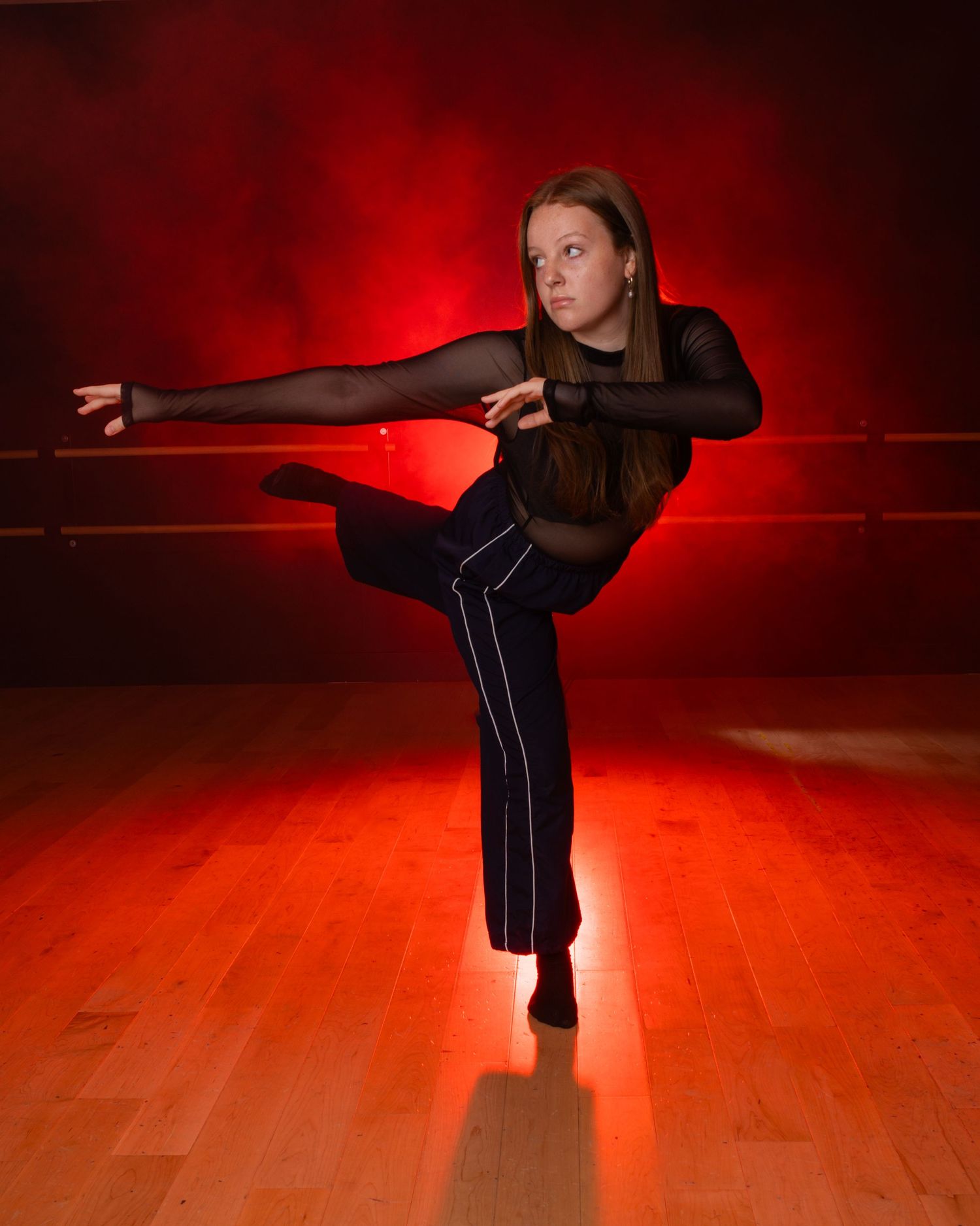 A martial arts student performs a graceful stance sequence in a red-lit studio with dramatic shadows.