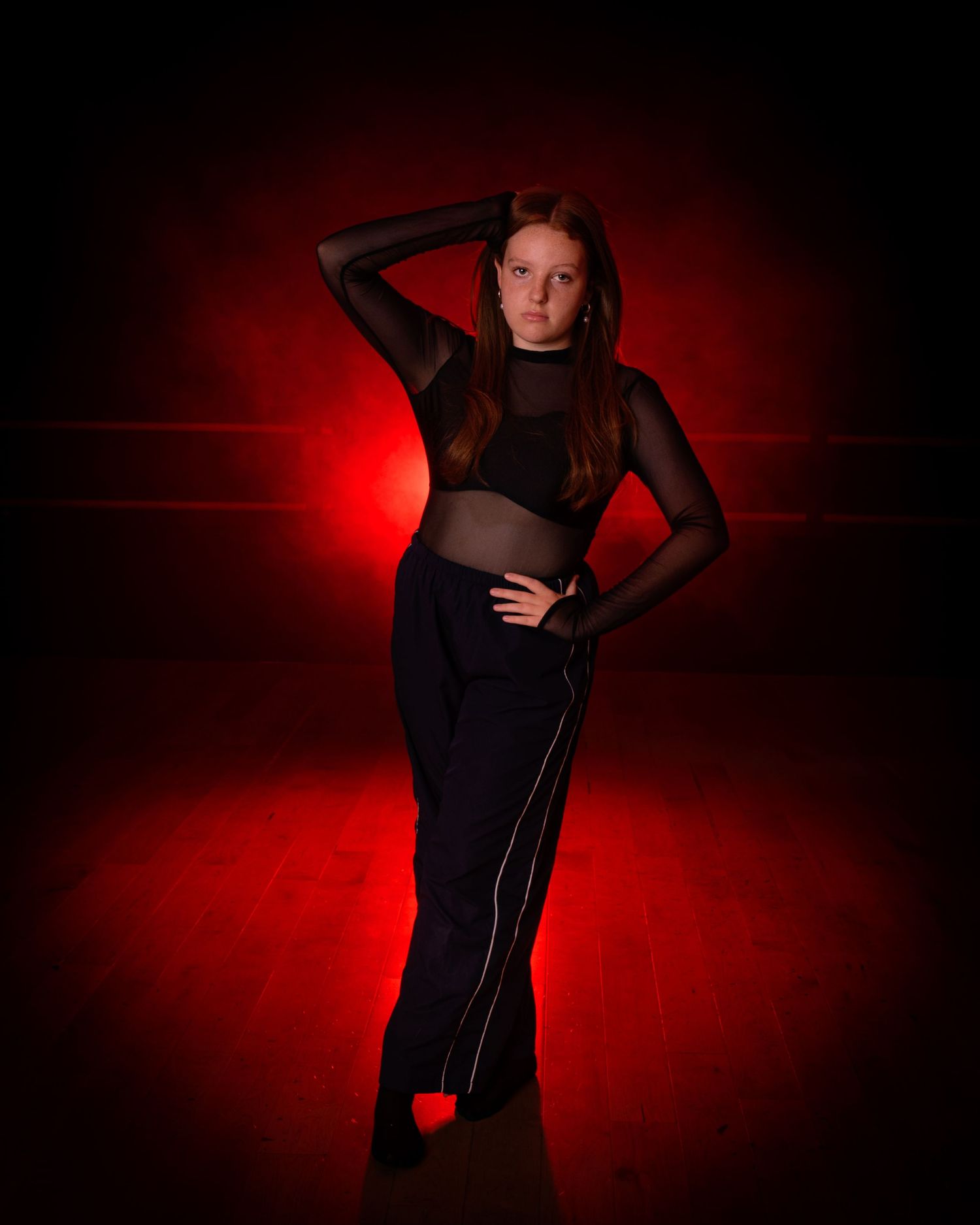 A dramatic silhouette of a person in dark clothing against a red backlit background in a dance-like pose.