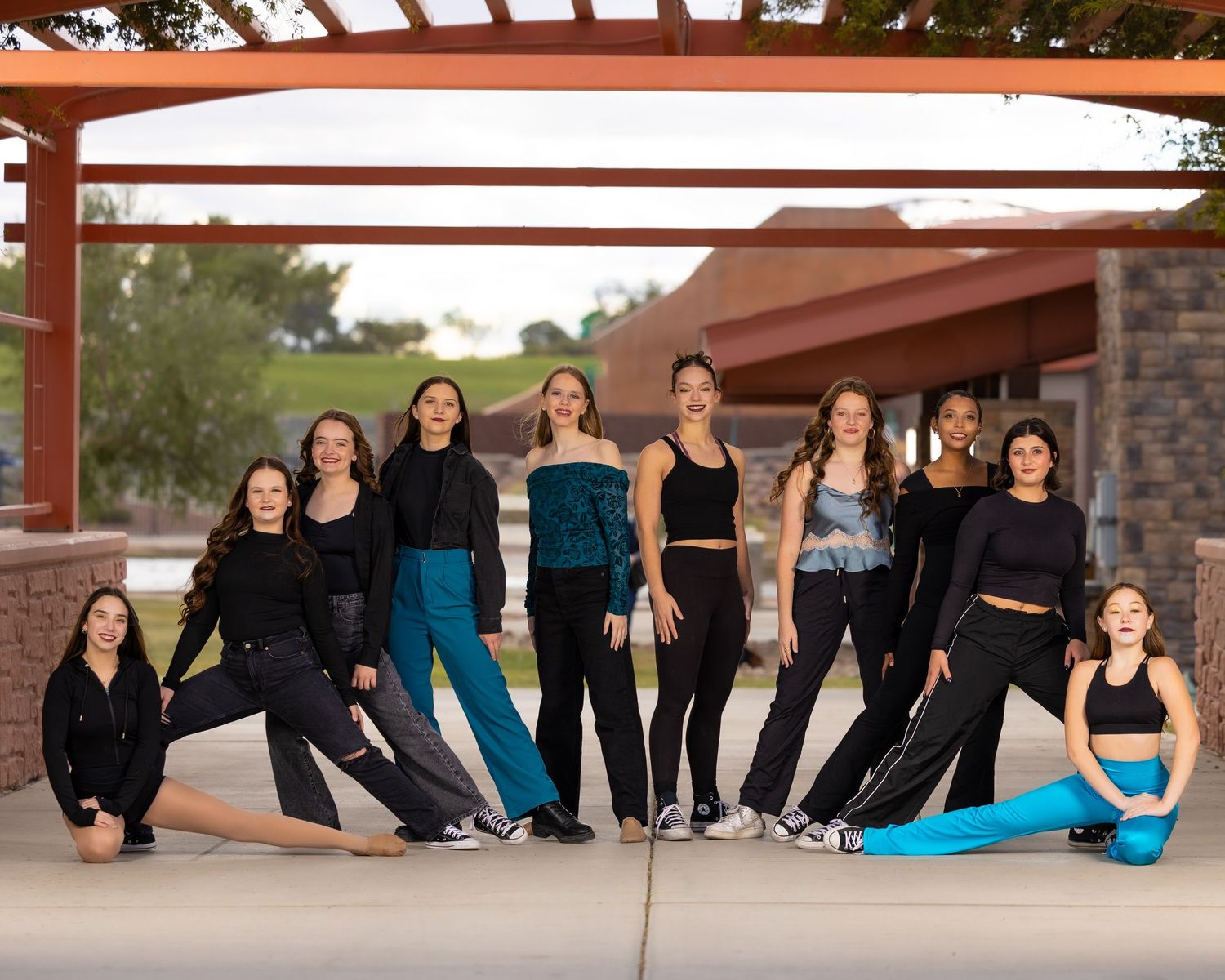 Dance group in matching black and blue outfits pose together for professional photographs outdoors.