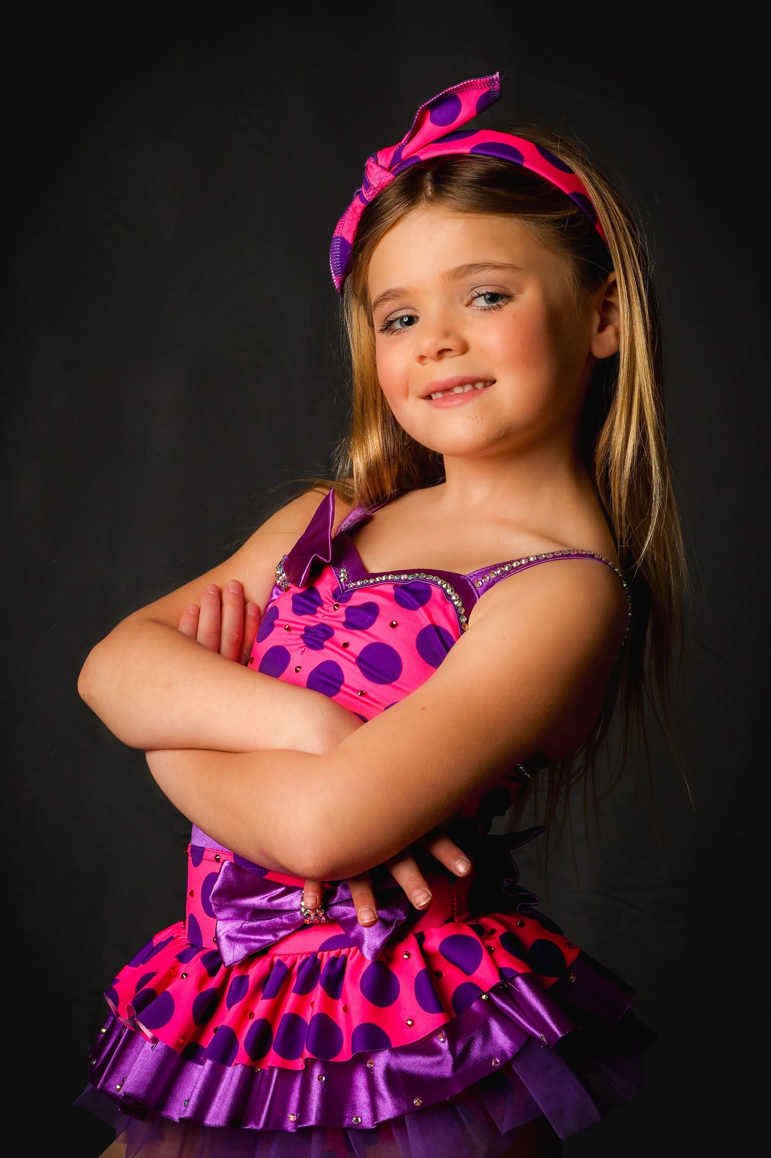 Black studio portrait featuring a vibrant pink and purple polka dot dress with ruffles against a dark background.
