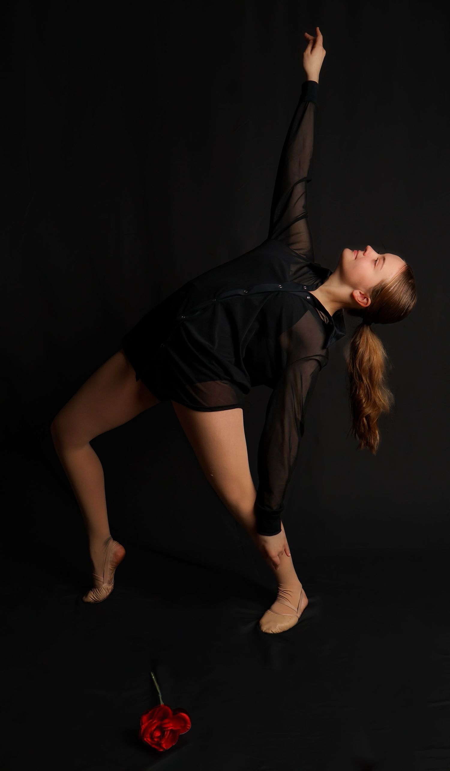 A dancer in a black sheer top performs a graceful contemporary dance sequence against a dark backdrop.