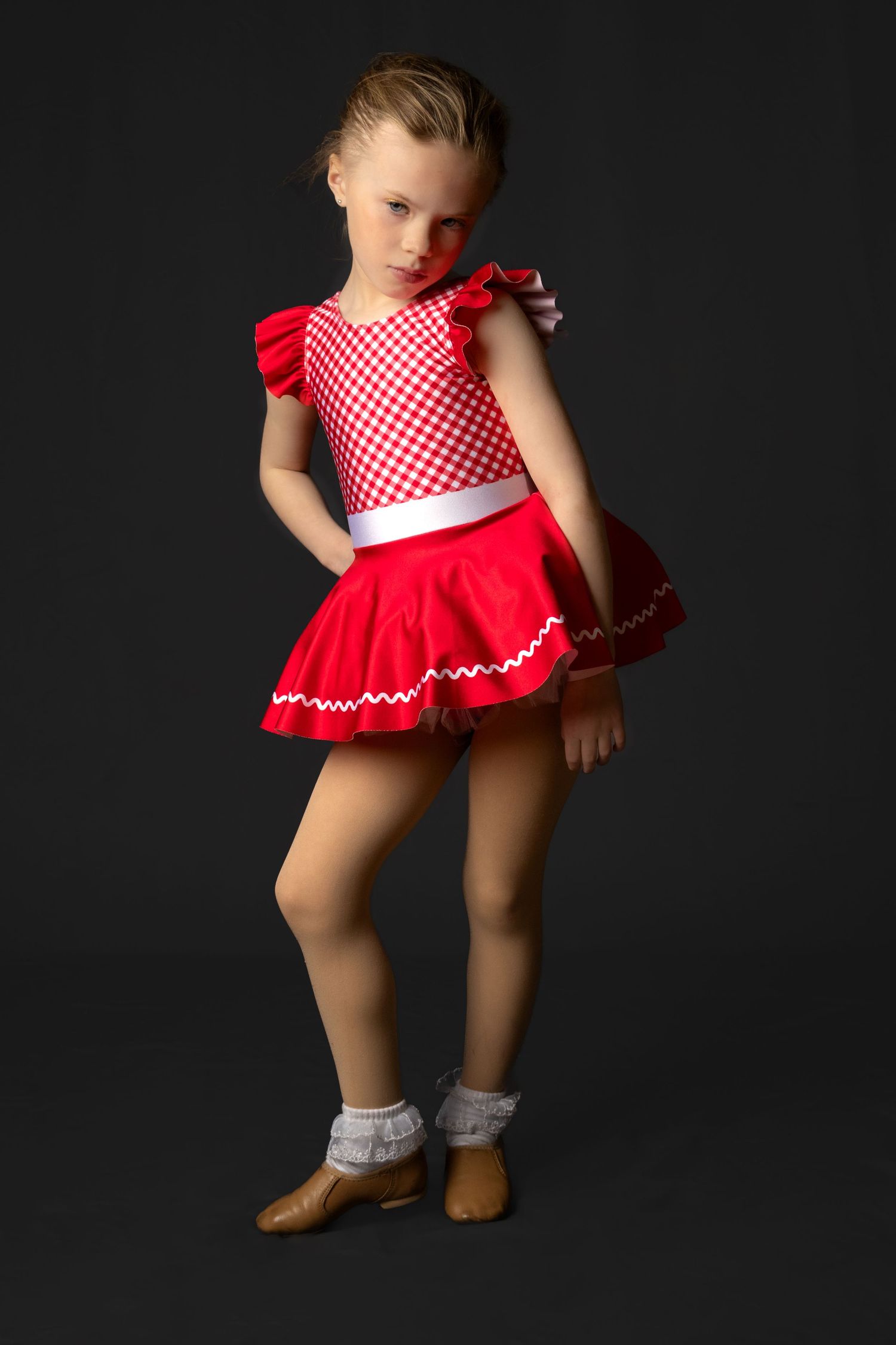 Child in red and white checkered dress with ruffled hem poses against dark background in five sequential dance positions.