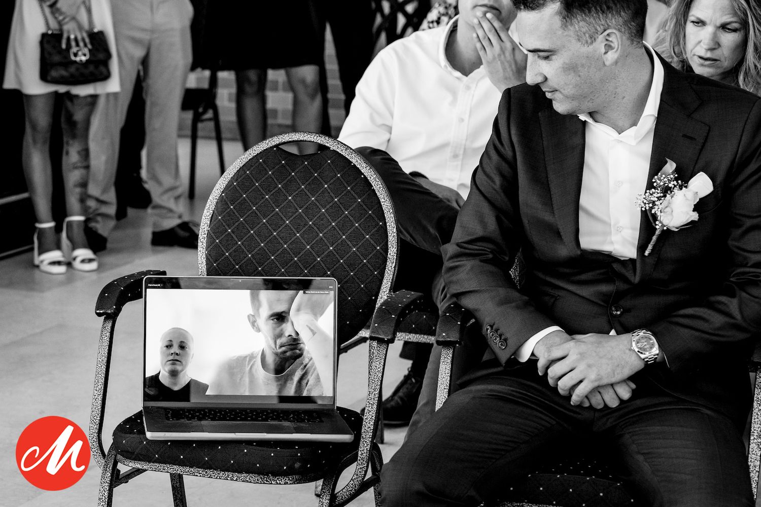 Wedding guests watch a video call on a mobile device propped on a chair during the ceremony.