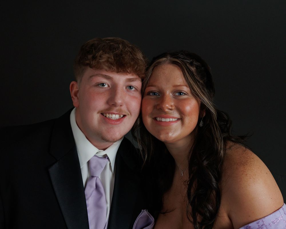A formal portrait photograph of a couple wearing black and pink formal attire against a dark background.