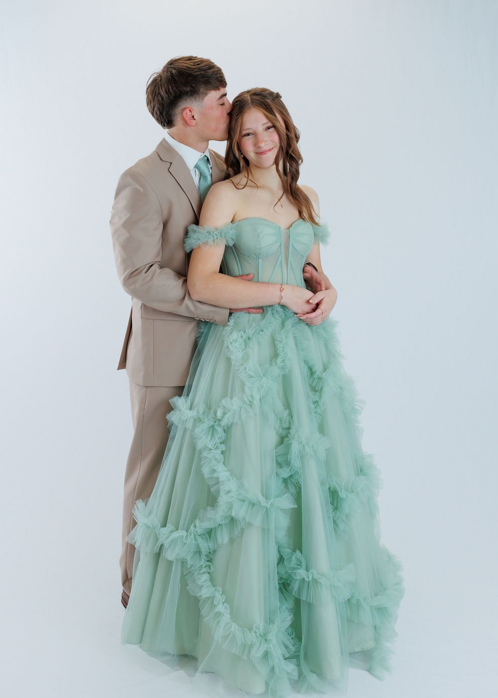 A couple embraces in a romantic photoshoot with her wearing a mint green tulle ballgown and him in a beige suit.
