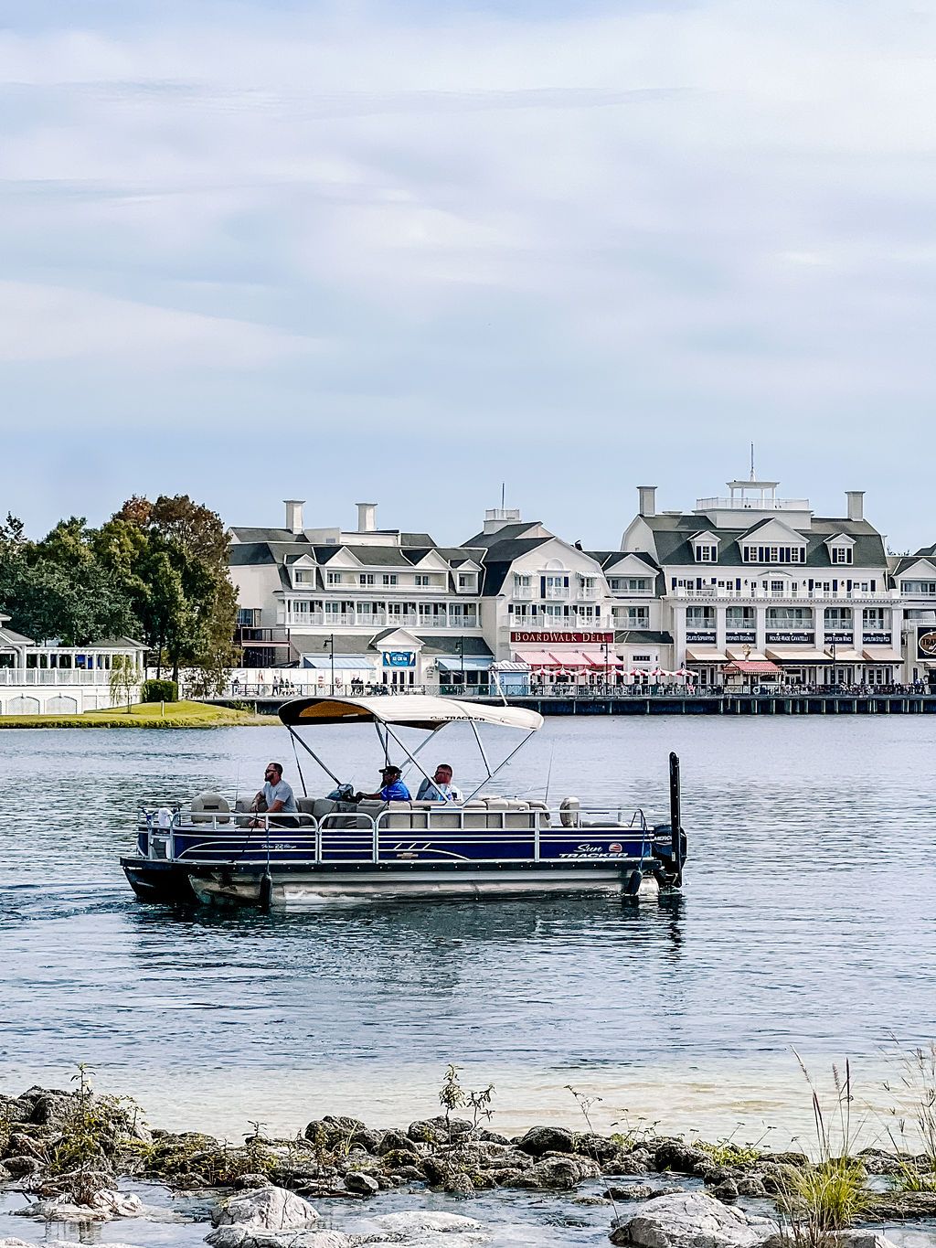 Pontoon boat cruises past waterfront resort buildings with white architecture.